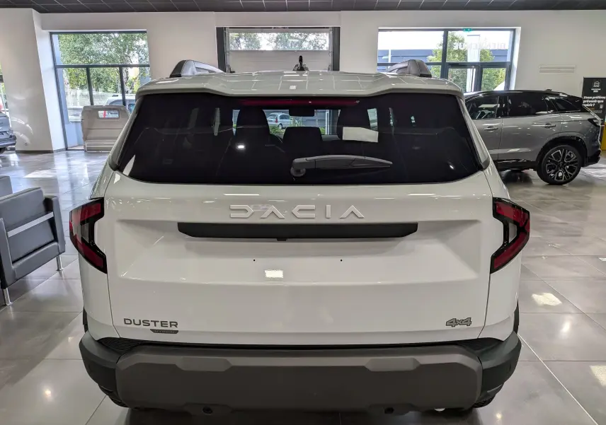 Vue arrière d'un Dacia Duster Hybrid-G blanc Glacier 4x4 en showroom, avec logo et feux arrière distinctifs.