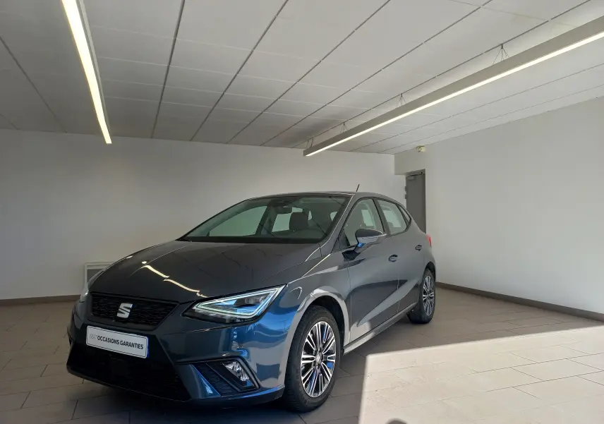 SEAT Ibiza 2025 gris magnétique vue 3/4 avant droit en intérieur avec jantes alliage et phares LED allumés.