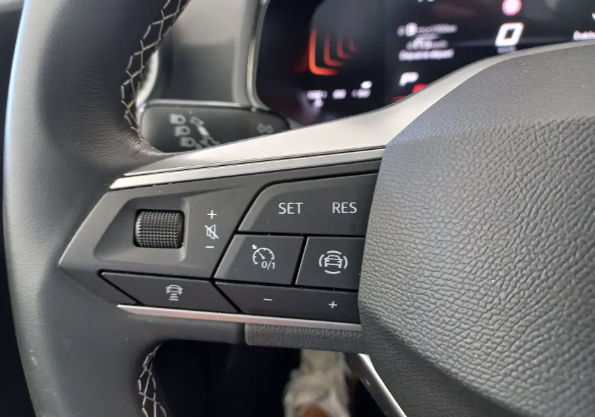 Gros plan sur les commandes au volant côté gauche du SEAT Ibiza 2025 gris magnétique, avec boutons de régulateur de vitesse et assistance.