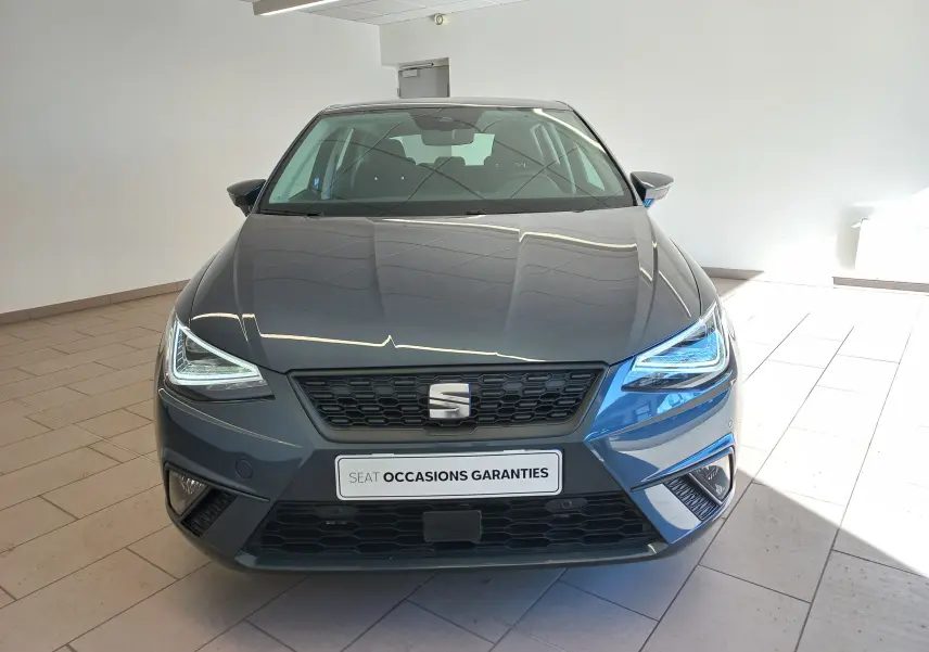 Vue frontale d'une SEAT Ibiza 2025 gris magnétique avec phares LED allumés et calandre noire en intérieur showroom.