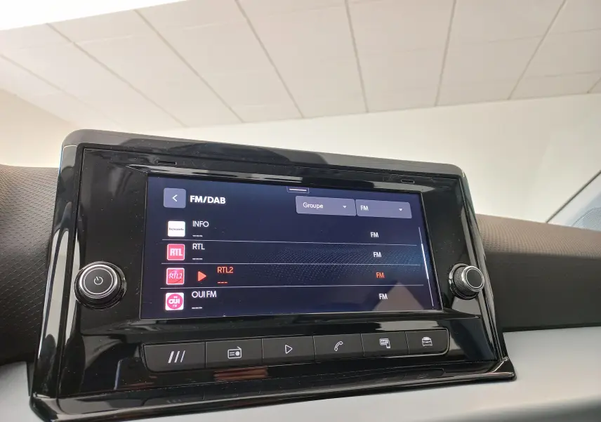 Écran tactile central de la SEAT IBIZA 2025 affichant les stations FM/DAB, entouré de boutons de contrôle noirs.