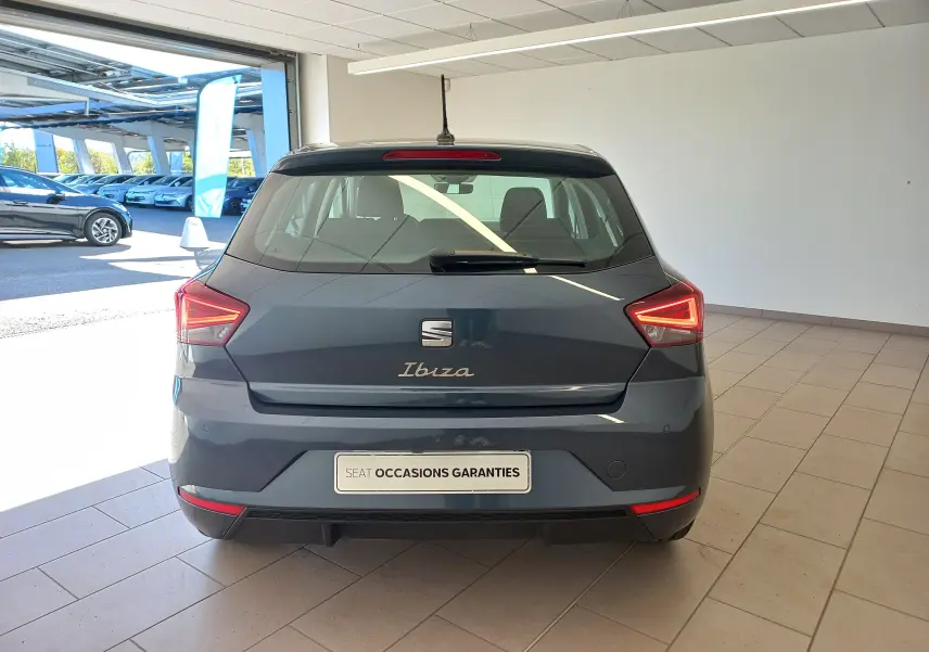 Vue arrière d'une SEAT Ibiza 2025 gris magnétique, avec feux arrière allumés et plaque "SEAT Occasions Garantis" visible.
