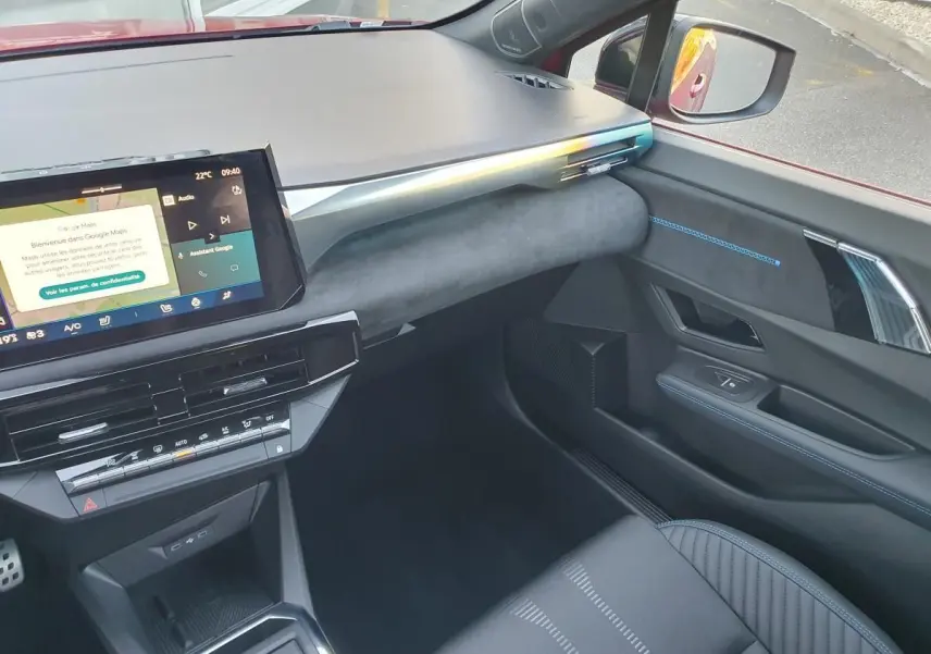 Vue intérieure côté passager de la Renault Clio VI rouge Absolu, avec tableau de bord moderne et écran tactile central.