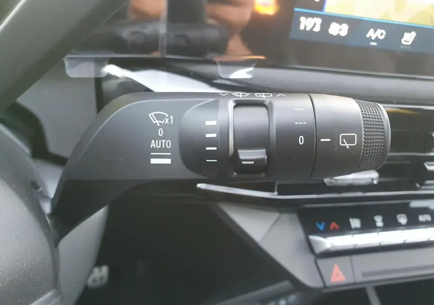 Gros plan sur la commande des essuie-glaces à gauche du volant dans l’habitacle de la Renault Clio VI rouge Absolu.