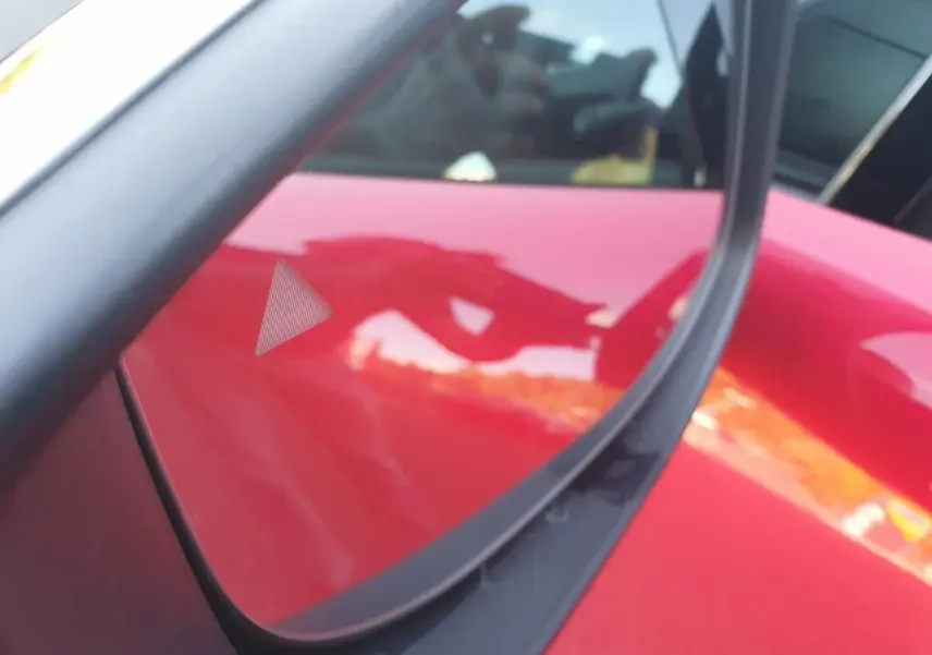 Détail du triangle d'alerte d'angle mort sur la porte côté gauche d'une Renault Clio VI rouge absolu.