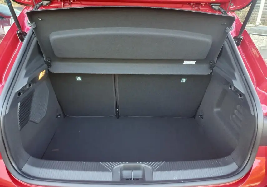 Coffre ouvert de la Renault Clio VI rouge absolu, vue arrière montrant l’espace de chargement vide et la tablette cache-bagages.