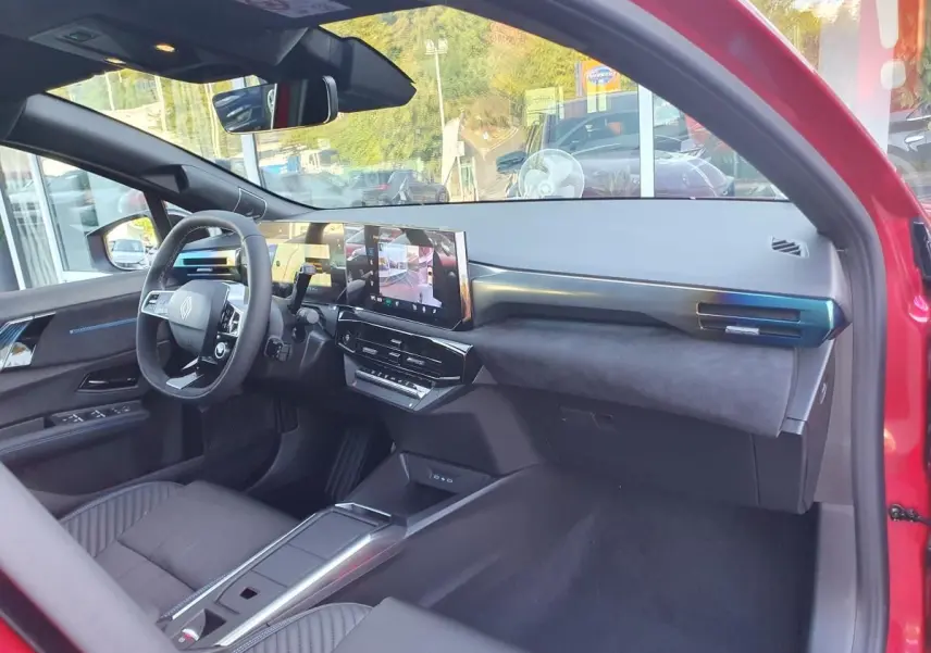 Vue intérieure côté conducteur de la Renault Clio VI rouge Absolu, avec tableau de bord moderne et écran tactile central.