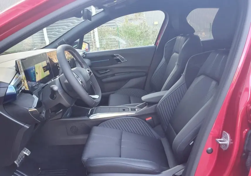 Vue intérieure côté conducteur de la Renault Clio VI rouge Absolu, sièges noirs et tableau de bord numérique.