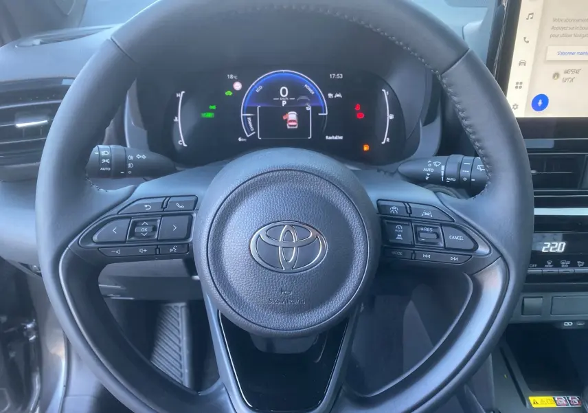 Vue rapprochée du volant cuir et du tableau de bord numérique de la Toyota Yaris Cross hybride gris atlas, année 2026.