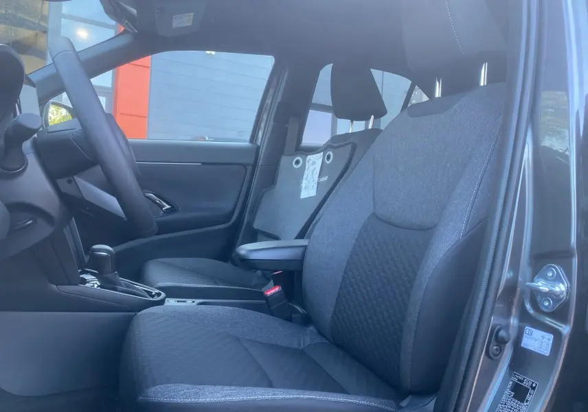Vue intérieure côté gauche des sièges avant gris tissu et volant cuir du Toyota Yaris Cross Hybride 130 Design Plus 2026.