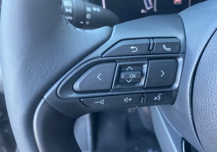 Gros plan sur les commandes multifonctions noires du volant cuir de la Toyota Yaris Cross hybride 130 Design Plus.