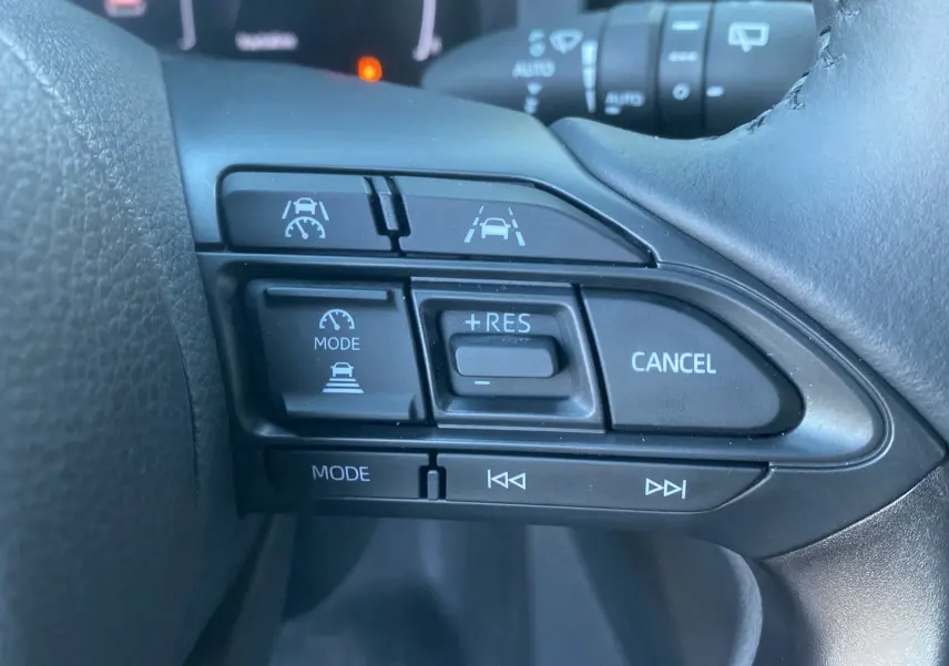 Gros plan sur les commandes au volant cuir noir de la Toyota Yaris Cross hybride 130 Design Plus 2026.