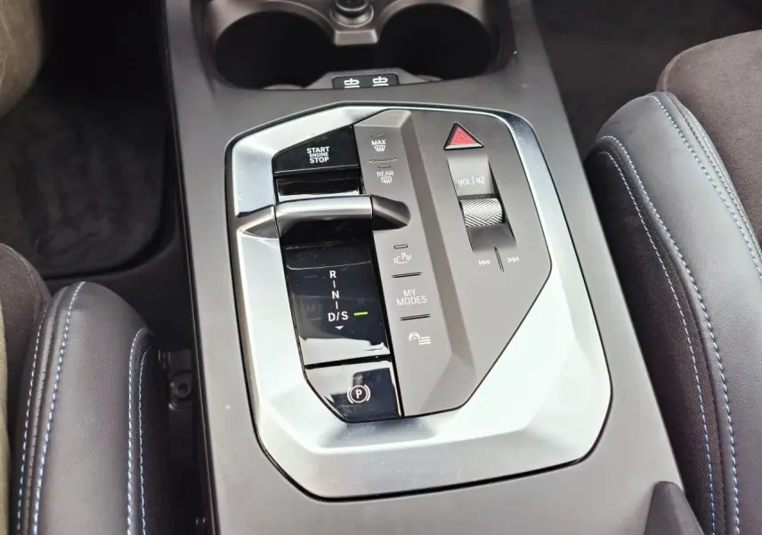 Vue rapprochée de la console centrale grise avec levier de boîte automatique et accoudoirs en Alcantara noir surpiqués bleus.