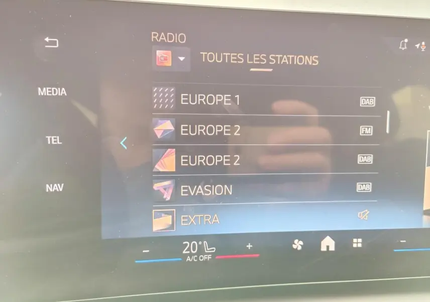 Écran tactile central de la BMW Série 1 2025 affichant les stations radio avec interface moderne et commandes climatisation.