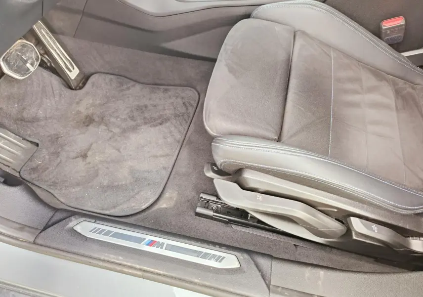 Vue intérieure côté conducteur de la BMW Série 1 M Sport 2025, siège Alcantara noir avec surpiqûres bleues et seuil M.