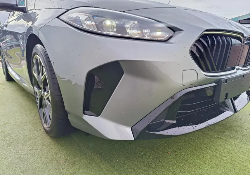 Gros plan sur la calandre noire et le capot gris Skyscraper d'une BMW Série 1 M Sport avec logo BMW visible.