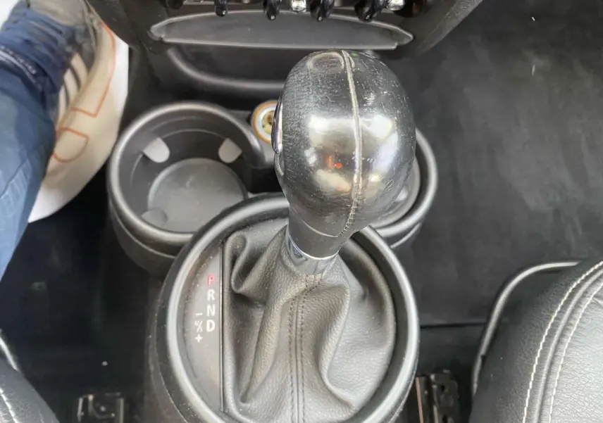 Le levier de vitesses automatique en cuir noir du MINI Countryman gris clair vu de dessus, avec porte-gobelets adjacent.