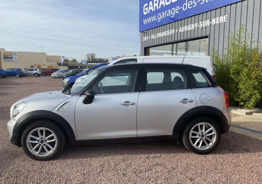 Vue de profil côté gauche d'une MINI Countryman gris clair avec toit noir, roues alliage et rétroviseurs noirs.