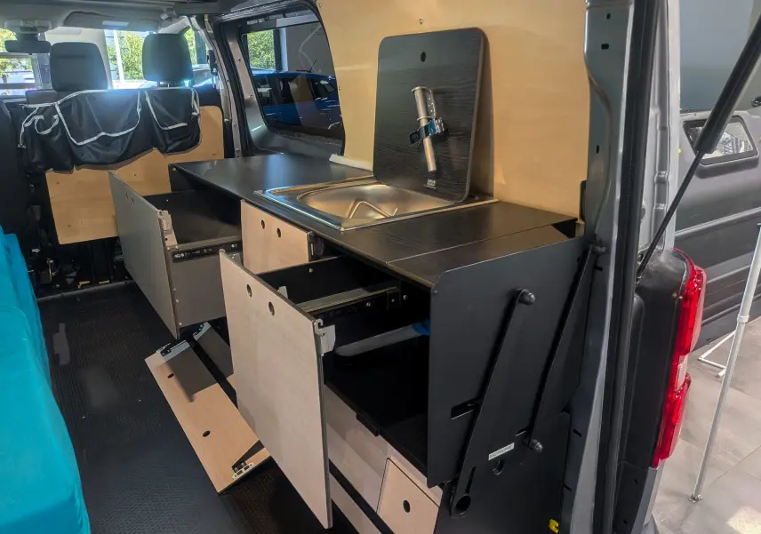 Vue intérieure côté droit du Peugeot Expert Fourgon gris acier aménagé avec cuisine intégrée en bois et rangements ouverts.