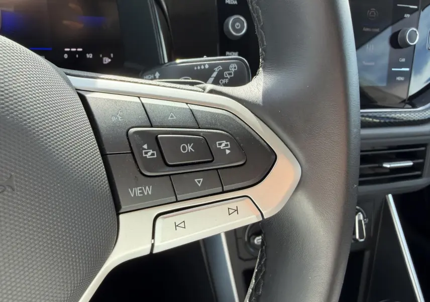 Gros plan sur les commandes multifonctions en cuir du volant du Volkswagen Taigo 2025, avec écran tactile en arrière-plan.
