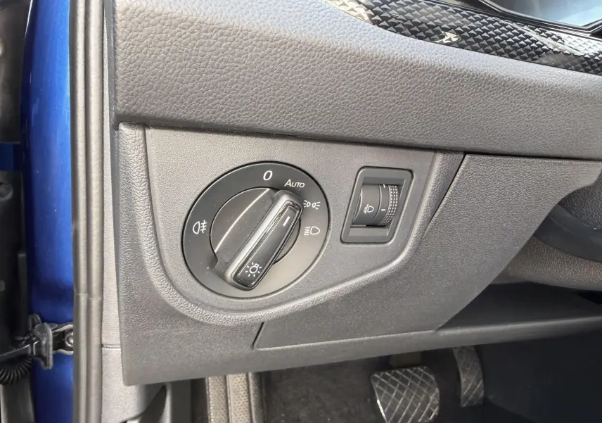 Vue intérieure côté gauche du tableau de bord bleu du Volkswagen Taigo 2025, avec commande des phares et réglage de l'éclairage.