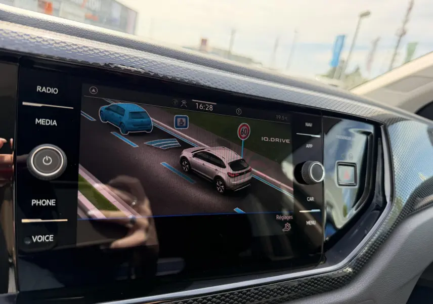 Écran tactile intérieur montrant l'assistance à la conduite avec vue 3/4 arrière d'une Volkswagen Taigo bleue.