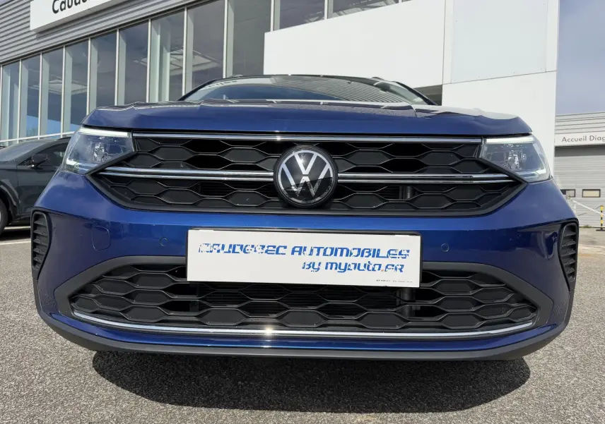 Vue frontale rapprochée d’un Volkswagen Taigo bleu métallisé avec calandre noire à motifs hexagonaux.