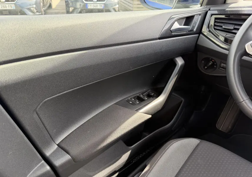 Intérieur côté conducteur du Volkswagen Taigo 2025, montrant la portière noire avec commandes des vitres et partie du volant cuir multifonctions.