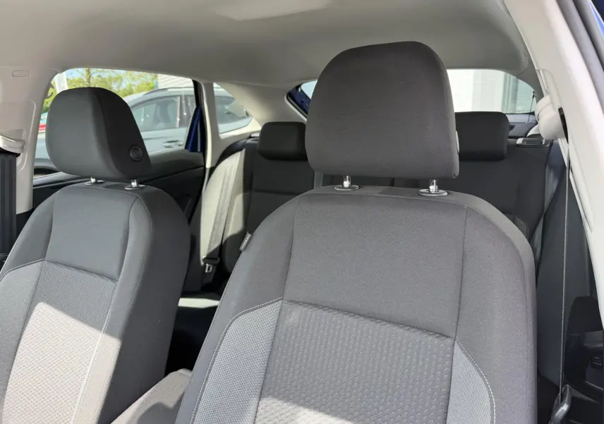 Vue intérieure des sièges avant et arrière en tissu gris du Volkswagen Taigo bleu, avec lumière naturelle entrant par la porte ouverte.