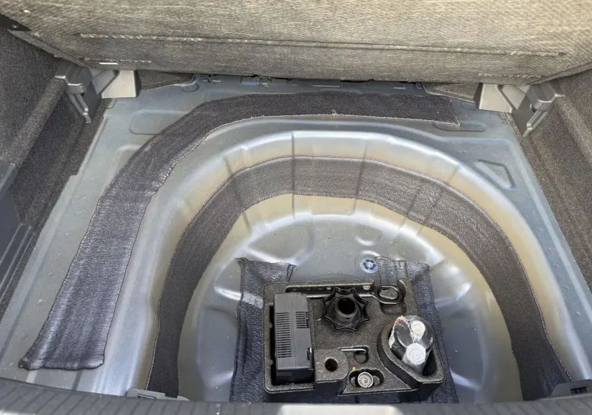 Coffre ouvert du Volkswagen Taigo bleu 2025, vue plongeante sur le rangement sous plancher avec kit de réparation pneus.