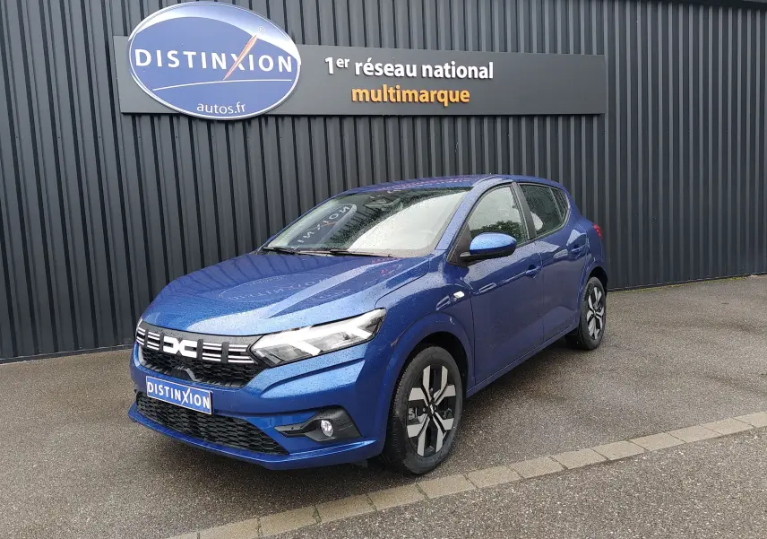 Dacia Sandero 2025 bleu Iron vue 3/4 avant droit avec jantes alliage et calandre distinctive sous pluie fine.