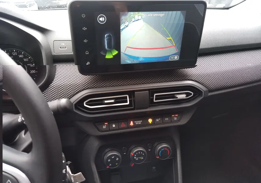Vue intérieure du tableau de bord de la Dacia Sandero 2025 avec écran tactile affichant la caméra de recul et commandes climatisation.