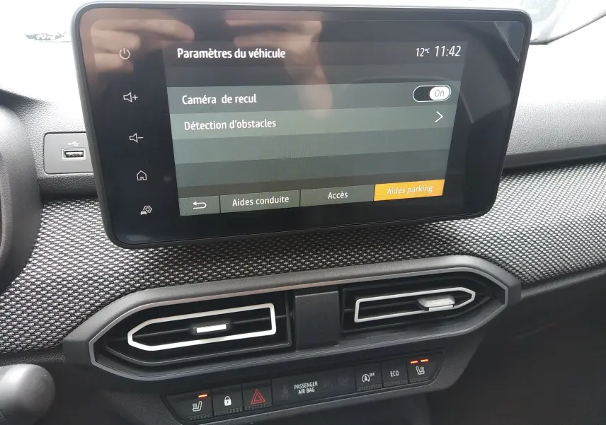 Écran tactile central affichant les paramètres d'aide au stationnement dans l'habitacle du Dacia Sandero bleu Iron 2025.