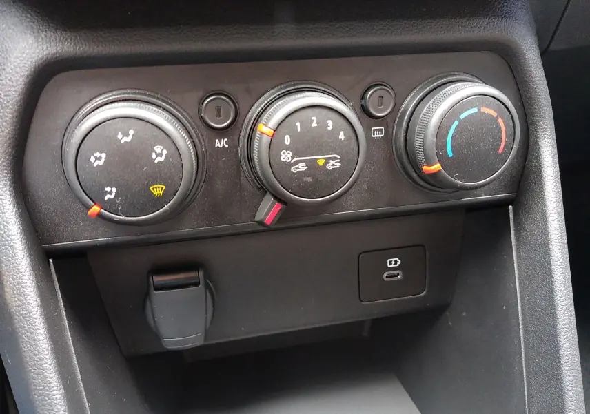Panneau de commande de climatisation avec trois molettes et port USB dans une Dacia Sandero bleu Iron 2025.