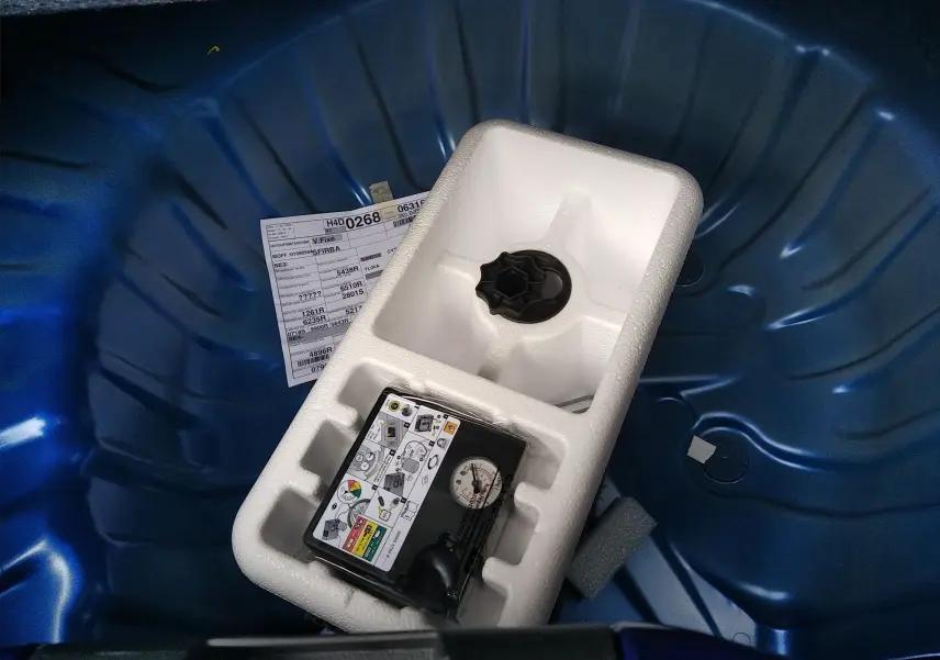 Gros plan sur le coffre bleu iron d'une Dacia Sandero 2025, montrant le logement de la roue de secours et un kit de réparation.