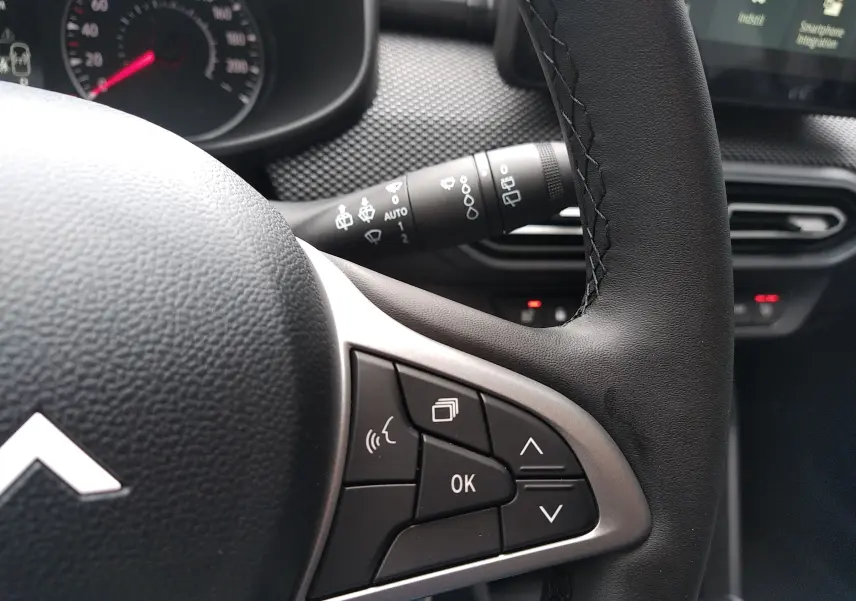 Gros plan sur le volant noir de la Dacia Sandero 2025 avec commandes multifonctions et tableau de bord partiel visible.