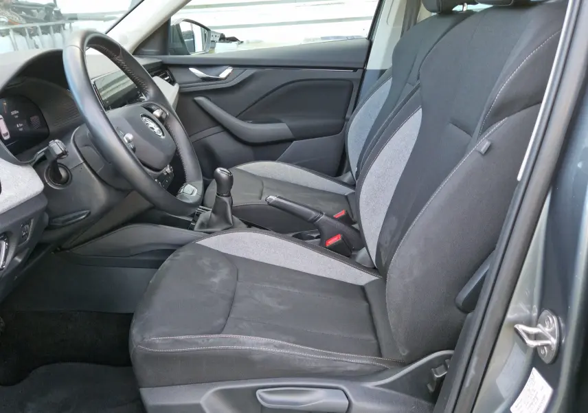 Intérieur côté conducteur d'un Skoda Kamiq 2024 gris graphite, sièges tissu gris et noir avec volant et levier manuel visibles.