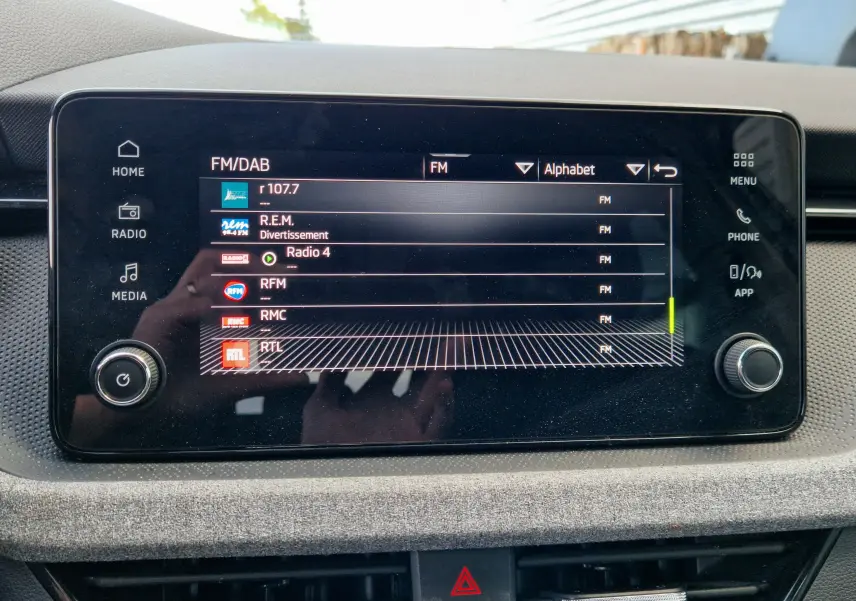 Écran tactile central du Skoda Kamiq 2024 affichant les stations radio FM avec commandes autour, intérieur gris.