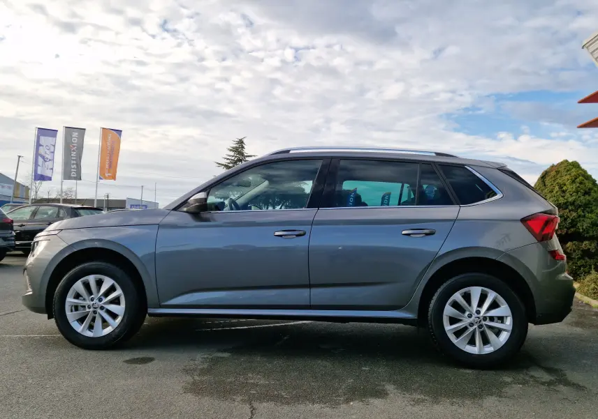 Vue de profil côté gauche d'un Skoda Kamiq gris graphite métal 2024 avec jantes alliage et toit ouvrant.