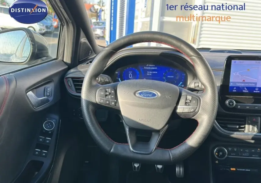 Vue intérieure centrée sur le volant perforé de la Ford Puma gris foncé avec tableau de bord numérique et écran tactile GPS.