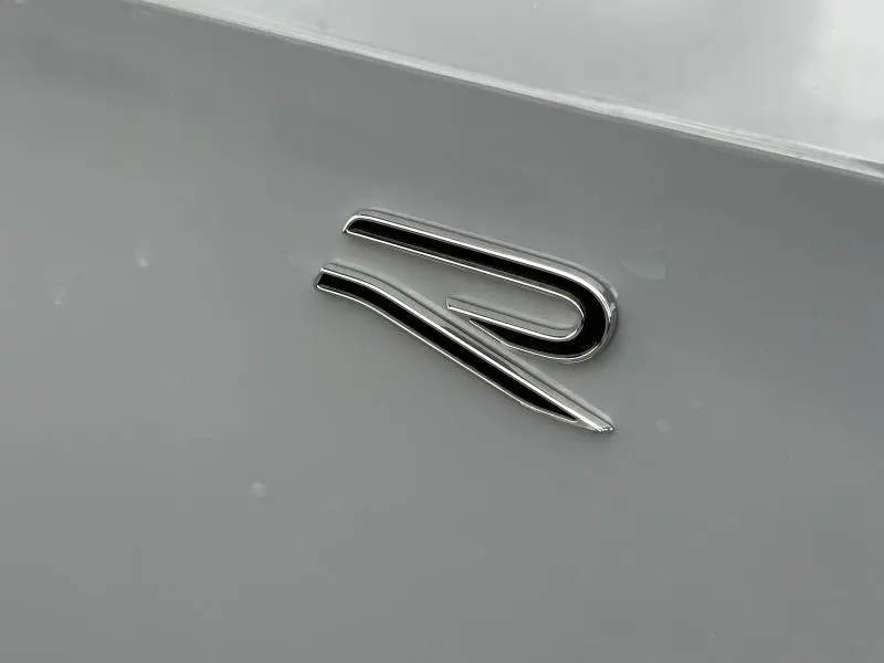 Gros plan sur l'emblème "R" chromé sur la carrosserie grise d'une Volkswagen Golf 2.0 TDI R-Line 2026.