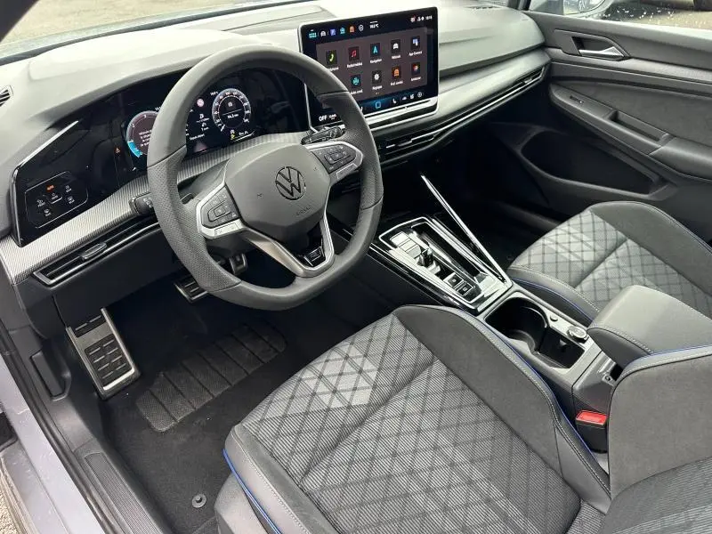 Vue intérieure côté conducteur de la Volkswagen Golf 2.0 TDI R-Line 2026 avec tableau de bord numérique et sellerie grise à surpiqûres bleues.