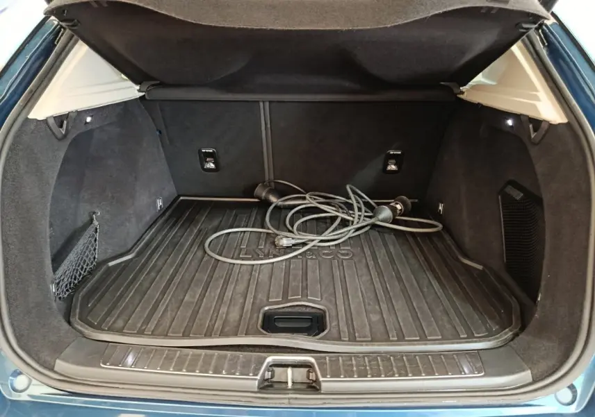 Coffre ouvert vu de l'arrière d'un Link & Co 01 bleu avec câble de recharge hybride posé sur le tapis de coffre.