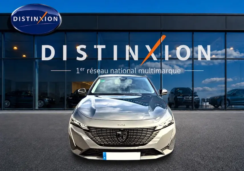 Vue avant d'une Peugeot 308 gris selenium garée devant une vitrine avec logo Distinxion.