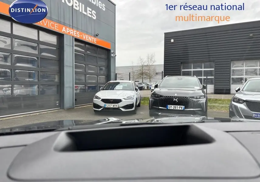 Vue depuis l'intérieur montrant le tableau de bord et par la vitre avant un Renault Austral noir étoile métal en 3/4 avant.