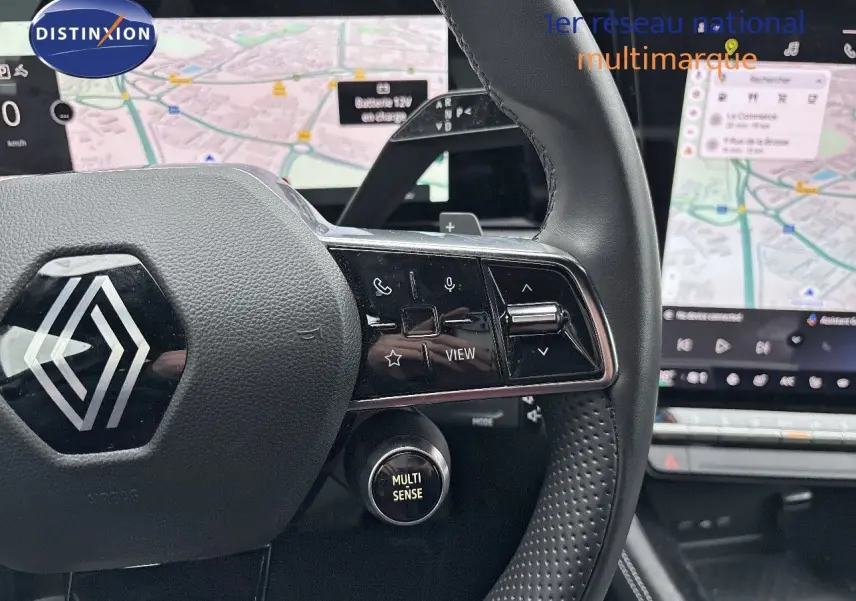 Gros plan sur le volant noir du Renault Austral 2023 avec commandes intégrées et écran tactile de navigation en arrière-plan.