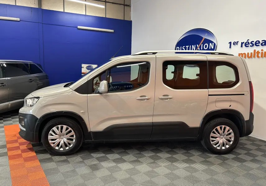 Profil côté gauche du Peugeot Rifter gris sable 2019 avec attelage, présenté en intérieur sur sol carrelé.