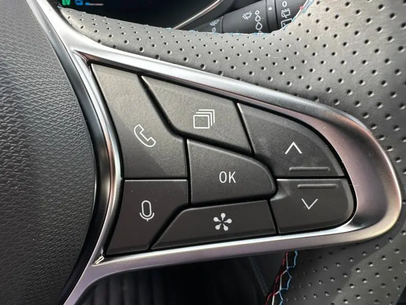 Gros plan sur les commandes multifonctions noires du volant perforé du Renault Captur 1.8 E-Tech Gris Rafale/Noir Etoilé 2026.