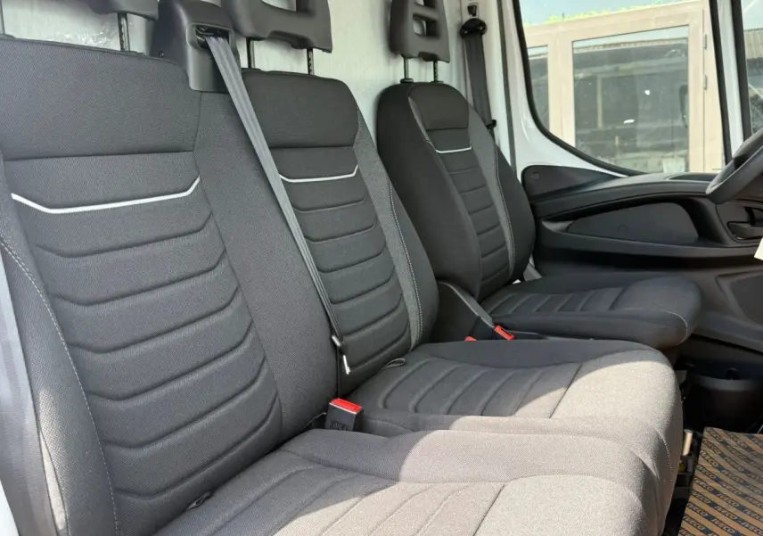 Vue intérieure côté conducteur du fourgon Iveco Daily 35S18 2026, montrant les sièges tissu gris foncé et la portière blanche.