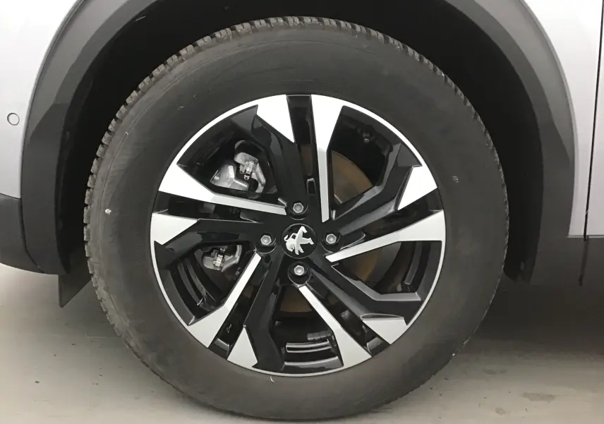 Gros plan sur la roue avant gauche du Peugeot 2008 électrique gris Artense, jante alliage noire et argentée au design moderne.